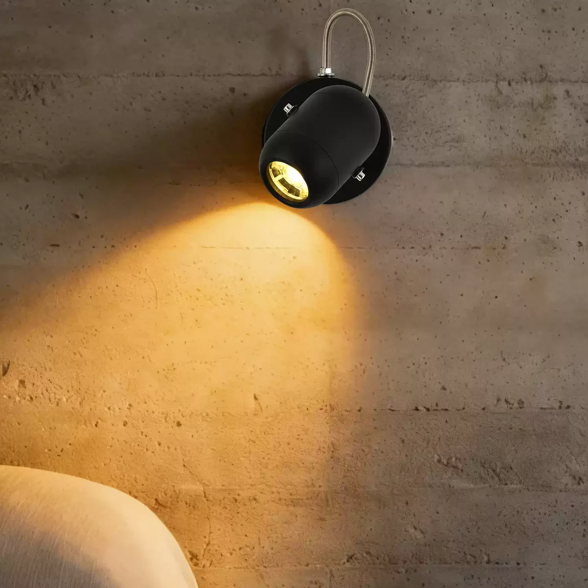 Black industrial wall spotlight with warm light on textured wall